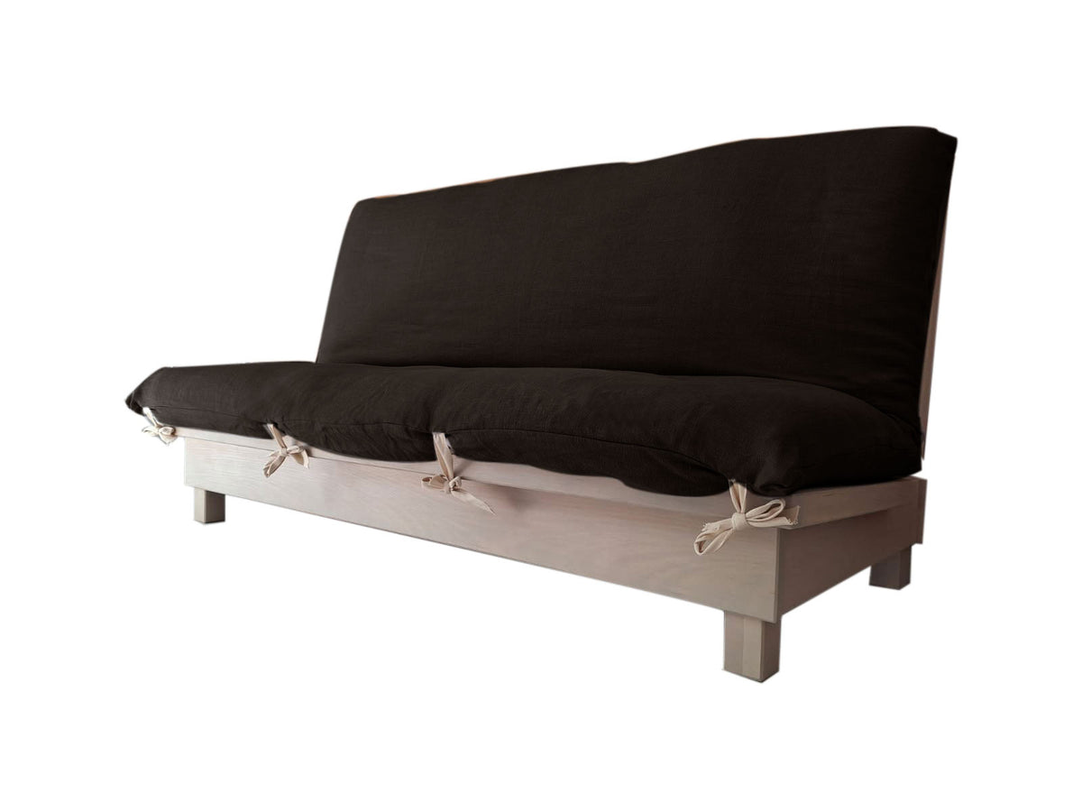 Banquette convertible en lit avec dossier relevé et coussins noirs sur une base en bois clair, ties décoratives sur le pourtour.